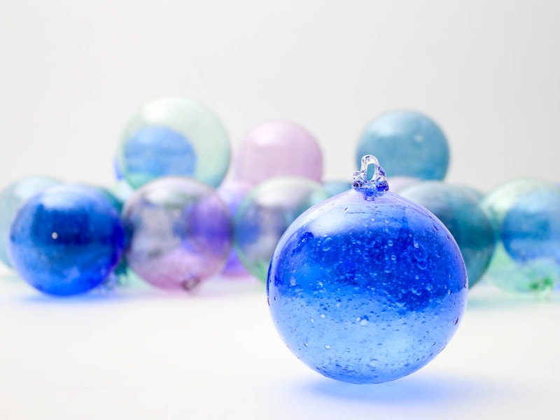 A blue bubbly handblown glass round ornament in front of an array of other colourful ornaments
