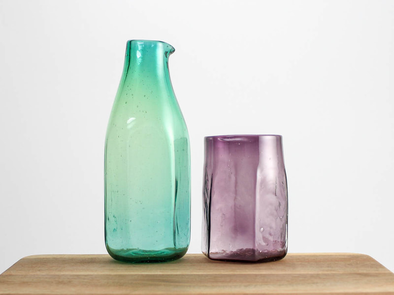 Handblown glass hexagon shaped green pitcher beside dark violet cup