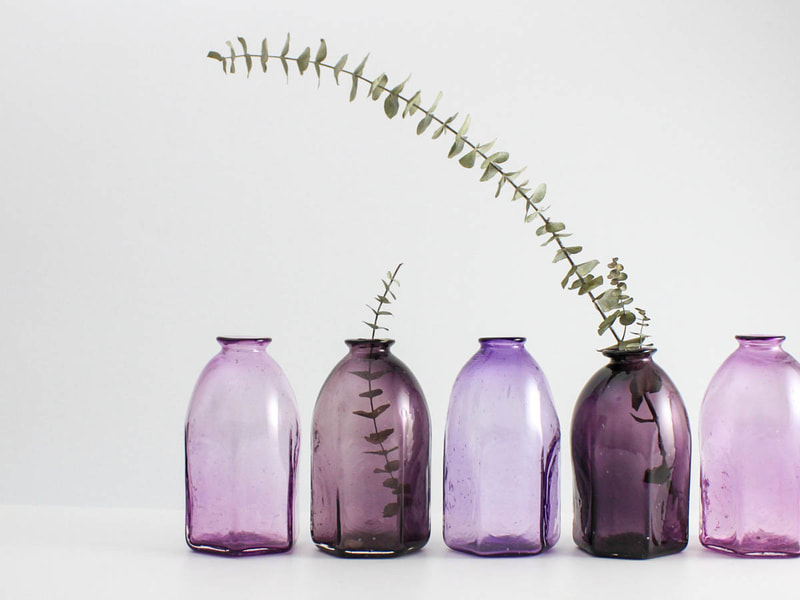 A row of hexagon shaped vases in different shades of purple with eucalyptus in them